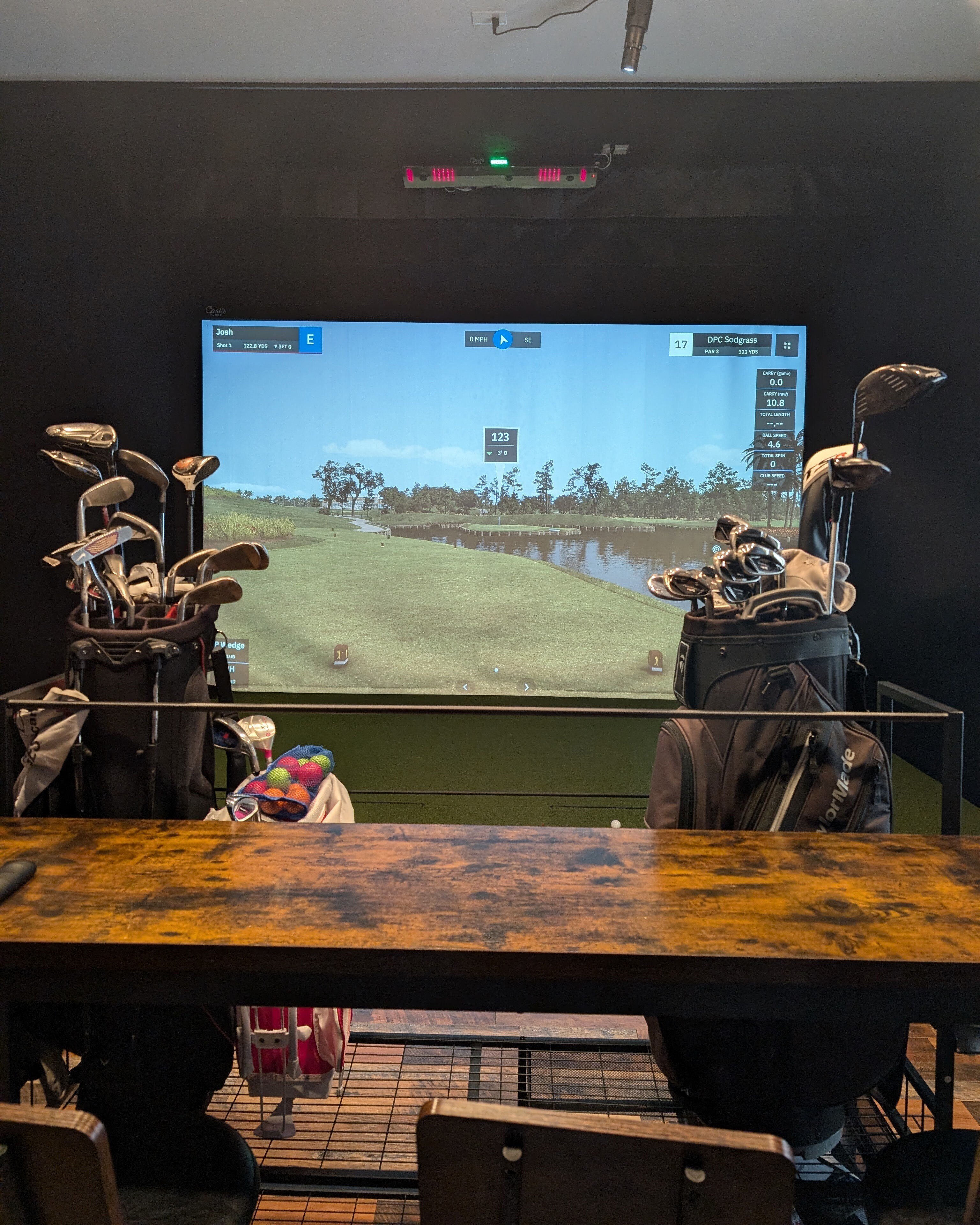Golf simulator bay with bar counter, golf bags, and storage near the spectator area