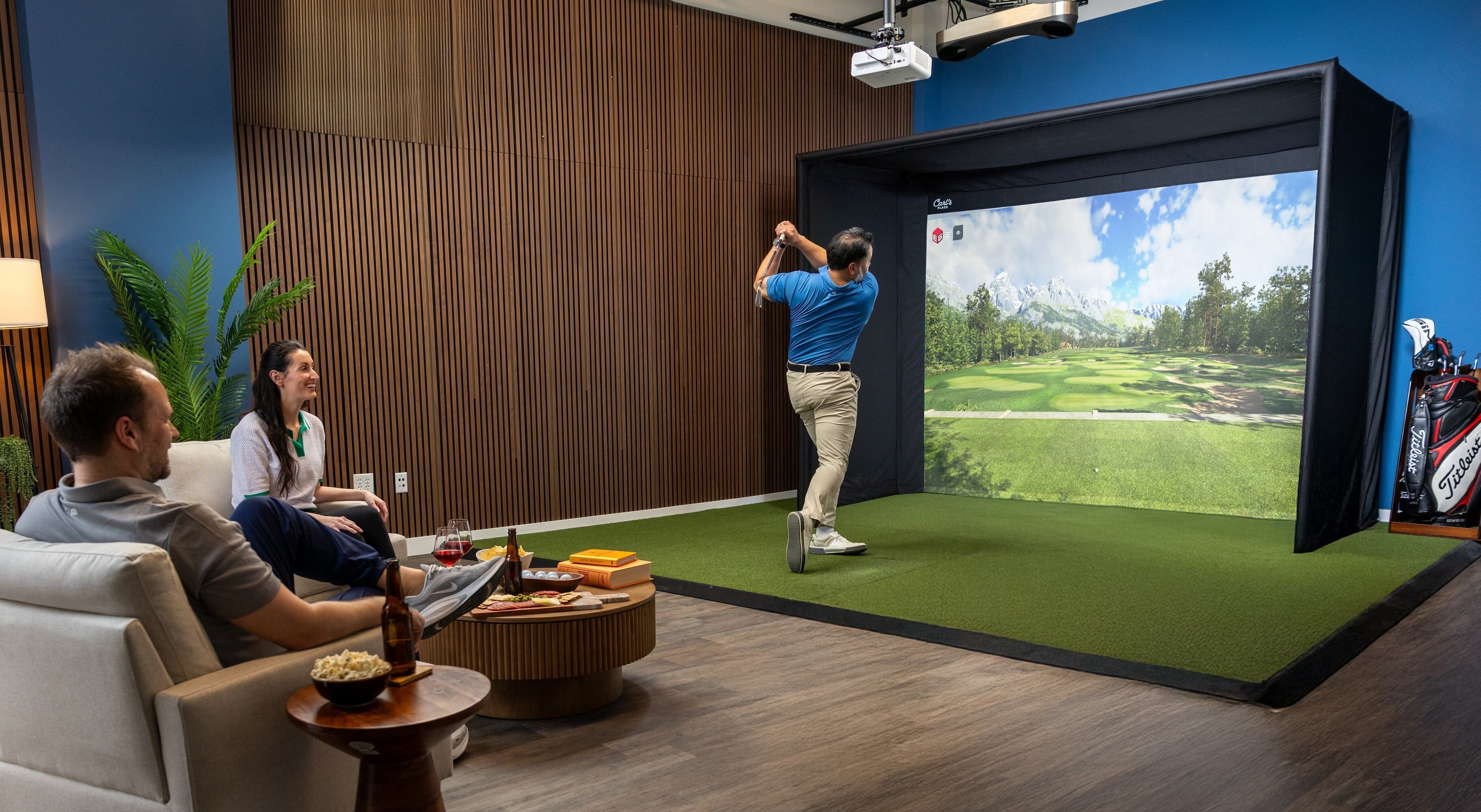 Golf simulator room with spectator seating and guests watching a golfer